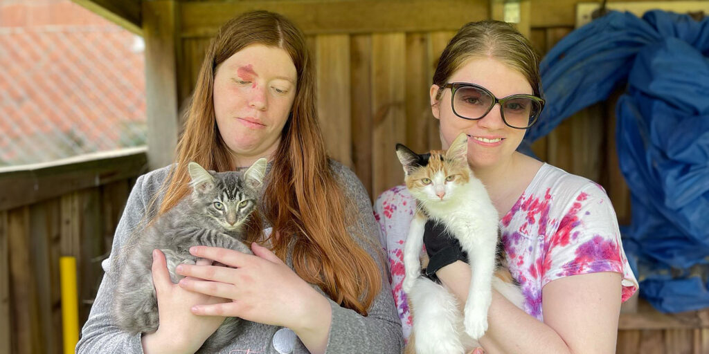 2 blonda tjejer med en varsin katt i famnen. 